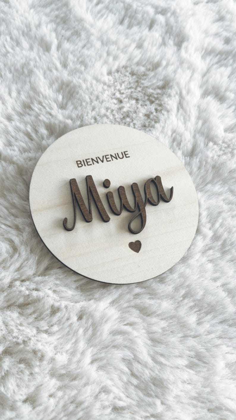 May include: A round wooden sign with the text "Bienvenue Miya" in cursive lettering and a small heart cutout.
