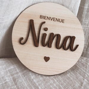 May include: A round wooden sign with the text "Bienvenue Nina" and a small heart.