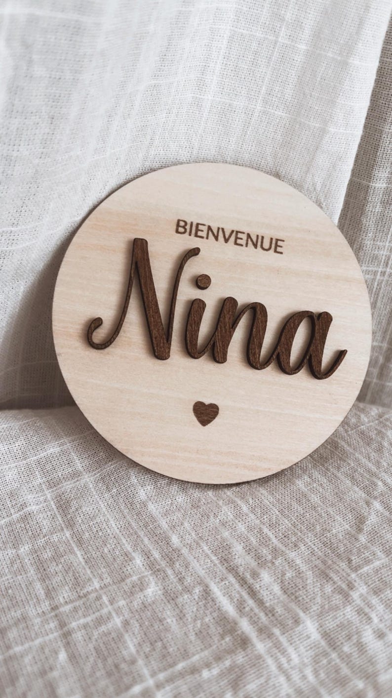 May include: A round wooden sign with the text "Bienvenue Nina" and a small heart.