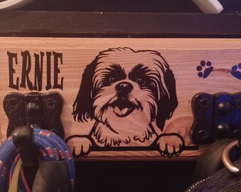 May include: Wooden dog leash holder with the name "ERNIE" in bold letters. The holder features a detailed illustration of a Shih Tzu dog and blue paw prints. Includes black hooks for leashes.
