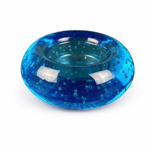 May include: A round, teal-colored glass candle holder with a bubble-like texture. The candle holder has a circular shape with a recessed center for a candle. The glass is transparent, allowing light to pass through, and is suitable for home decor.
