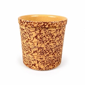May include: A cylindrical ceramic crock featuring a tan base color with a dense, dark brown sponge-painted or mottled pattern covering the exterior surface. The vessel has a smooth, rounded rim and a wide, open top, presenting a uniform shape.