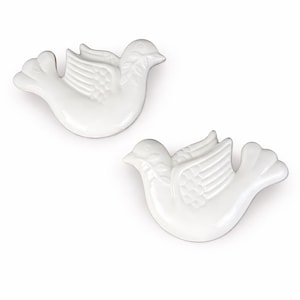 May include: Two white ceramic dove figurines. Each dove has detailed wings and tail feathers. The doves are positioned on a white background. The figurines are likely decorative items.