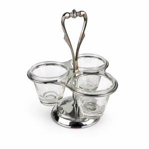 May include: A silver-toned condiment server with three clear glass cups. The server has a handle with a heart-shaped design and a circular base. The cups are held in place by a silver metal frame.