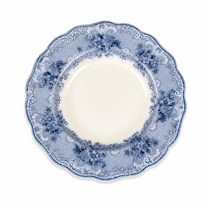 May include: A round ceramic dinner plate with a scalloped edge, featuring a cream-colored center and a wide border decorated with a blue and white floral pattern, intricate lace-like detailing, and scrolling foliage motifs throughout the rim.