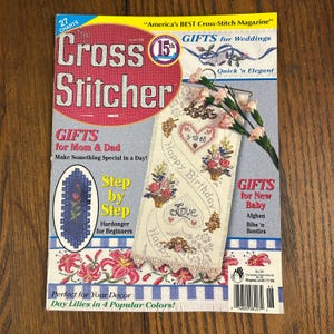 May include: A copy of "Cross Stitcher" magazine with a pink and red cover. The cover features text and images related to cross-stitch projects, including gifts for various occasions. The magazine also includes step-by-step instructions for beginners.