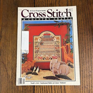 May include: A vintage issue of "Cross Stitch & Country Crafts" magazine. The cover features a cross-stitch sampler with Noah's Ark, animals, and an alphabet. The magazine has a white price tag on the side.