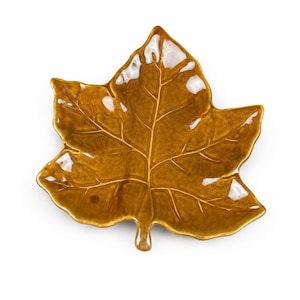 May include: A ceramic leaf-shaped dish in a warm, golden-brown color. The dish has a glossy finish and detailed veining, resembling a maple leaf. The leaf dish is a decorative item, suitable for serving or display.