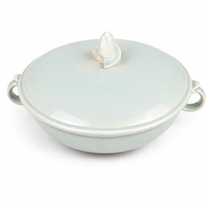 May include: A light blue ceramic serving dish with a matching lid. The lid features a decorative floral-shaped handle. The dish has two loop handles on either side. The overall design is simple and elegant.