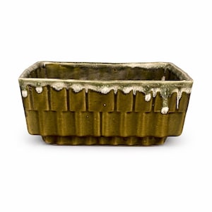 May include: A rectangular, olive green ceramic planter with a textured, brick-like pattern. The rim features a dripped, off-white glaze. The planter is a decorative item for indoor or outdoor use.