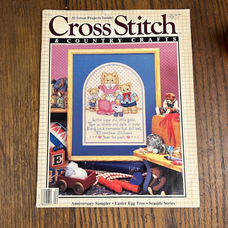 May include: A vintage "Cross Stitch & Country Crafts" magazine cover. The cover features a cross-stitch sampler with teddy bears and the text "Little boys and little girls, tour on wheels and dolls in curls..." Other items include wooden toys and books.