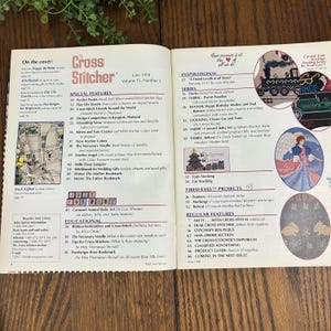 May include: Open magazine spread featuring the cover of "Cross Stitcher" magazine, June 1998 issue. The pages display articles on cross-stitch projects, including banners, stockings, and baby sets. The magazine's cover features a cross-stitch design.