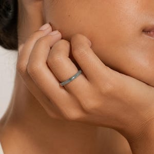 May include: A smooth, solid grey band ring with a rounded profile. The ring features a simple, continuous circular design with a matte finish, worn on the ring finger. The band has a uniform thickness and a clean, unadorned surface throughout.