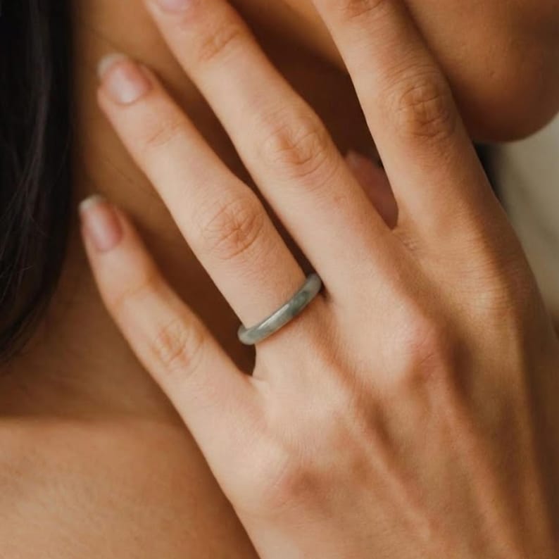 May include: A jade ring with a smooth, polished surface. The ring is a pale green color and is worn on a finger. The ring is a simple band design.