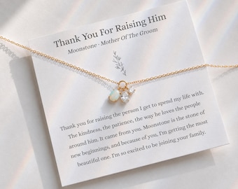 May include: A gold-tone chain necklace featuring a small pendant with an oval moonstone and two clear crystals. The necklace is displayed on a white card printed with the text Thank You For Raising Him, Moonstone, Mother Of The Groom.