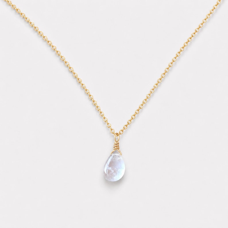 May include: A delicate gold chain necklace featuring a single, translucent, teardrop-shaped gemstone pendant. The stone is secured with gold wire wrapping at the top, creating a simple, elegant drop design that hangs centrally from the fine metal links.