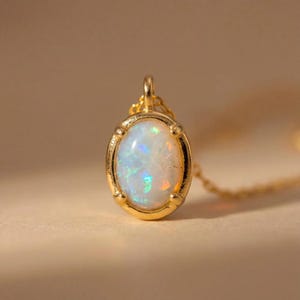 May include: A gold pendant necklace featuring an oval opal gemstone. The opal displays a play of color with iridescent flashes of blue, green, and orange. The pendant is set in a gold bezel with a delicate chain.
