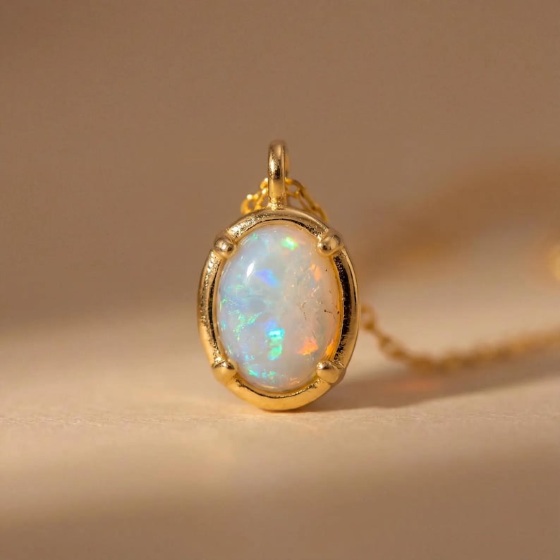 May include: A gold pendant necklace featuring an oval opal gemstone. The opal displays a play of color with iridescent flashes of blue, green, and orange. The pendant is set in a gold bezel with a delicate chain.