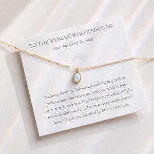 Pode incluir: Um colar de corrente em tom dourado com um pingente de opala oval centrado num cartão de apresentação branco. O cartão apresenta o texto: TO THE WOMAN WHO RAISED ME, Opal - Mother Of The Bride, e uma mensagem de gratidão.