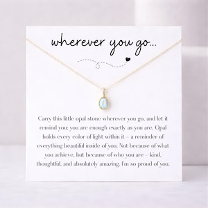 May include: A gold-colored necklace with a small, oval, light blue opal pendant. The necklace is displayed on a white card with the text "wherever you go..." and a message about self-worth.