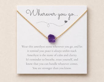 Könnte beinhalten: Eine goldfarbene Kette mit einem einzelnen, rohen, tiefvioletten Amethyst-Anhänger. Die Kette ist auf einer weißen Karte befestigt, die den Text "Wherever you go..." sowie eine gedruckte Botschaft über Frieden, Ruhe und Klarheit enthält.