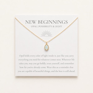 Op de afbeelding: Een gouden ketting met een kleine ovale opaal hanger op een witte kaart. De kaart bevat de tekst NEW BEGINNINGS OPAL | POSSIBILITY & LIGHT, een tekst over opaal en een icoon van een zonnetje boven de ketting.