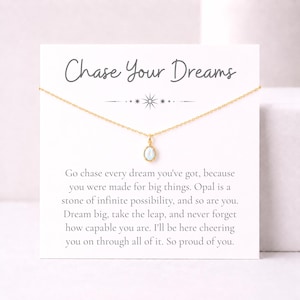 May include: A gold chain necklace with a small oval opal pendant displayed on a white card. The card features the text "Chase Your Dreams" at the top and an inspirational message below, including the phrase "Opal is a stone of infinite possibility."