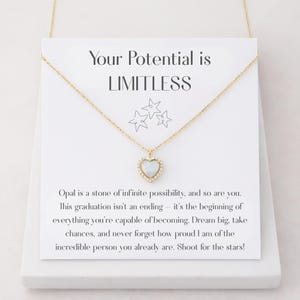 May include: A gold-toned necklace with a heart-shaped opal pendant, surrounded by small crystals. The pendant hangs from a delicate chain. The necklace is displayed on a white card with the text "Your Potential is LIMITLESS".