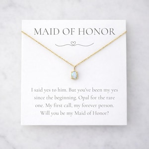 Könnte beinhalten: Eine goldfarbene Halskette mit einem rechteckigen Opalanhänger auf einer weißen Karte. Auf der Karte steht "MAID OF HONOR" über einem Herzdesign, mit dem Text "Will you be my Maid of Honor?"