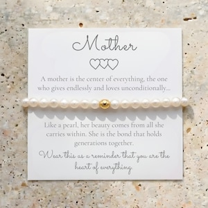May include: A pearl bracelet with a gold bead is displayed on a white card with the word "Mother" and a message about motherhood. The bracelet is made of small, round, white pearls.
