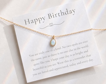 Puede incluir: Un collar de cadena en tono dorado con un pequeño colgante de ópalo iridiscente de forma ovalada. El collar se presenta sobre una tarjeta blanca con el texto Happy Birthday y un mensaje impreso sobre ser único, brillante y hermoso.