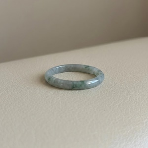 May include: A jade ring with a smooth, polished surface. The ring is a pale green color with darker green marbling throughout. The ring is a simple band design.