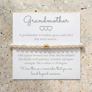May include: A pearl bracelet with a gold bead is displayed on a white card. The card reads "Grandmother" with a message about love and family. The bracelet is a delicate piece of jewelry.