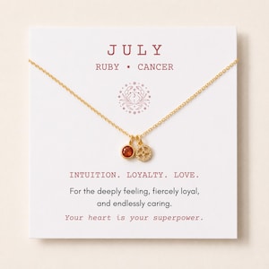 May include: A gold-tone necklace with two small charms, one featuring a round red stone and the other a circular cutout design, displayed on a white card labeled JULY, RUBY, CANCER, with text reading INTUITION. LOYALTY. LOVE. For the deeply feeling, fiercely loyal, and endlessly caring. Your heart is your superpower.