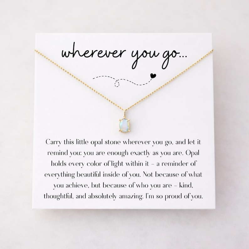 Puede incluir: Un collar dorado con un colgante de &oacute;palo rectangular sobre una tarjeta blanca. La tarjeta tiene el texto "wherever you go..." y un mensaje sobre la autoestima. Una joya delicada.