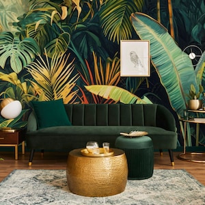 Peut inclure: Un canap&eacute; en velours vert avec des pieds dor&eacute;s est plac&eacute; devant une fresque murale repr&eacute;sentant une jungle tropicale. Une table basse ronde dor&eacute;e avec une finition martel&eacute;e et un ottoman en velours vert se trouvent devant le canap&eacute;. Une table d'appoint dor&eacute;e avec un plateau en verre et une plante en pot se trouvent &agrave; droite du canap&eacute;.