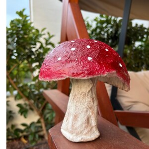 May include: A red and white mushroom garden statue with white polka dots on the top. The mushroom has a white stem with a textured surface.