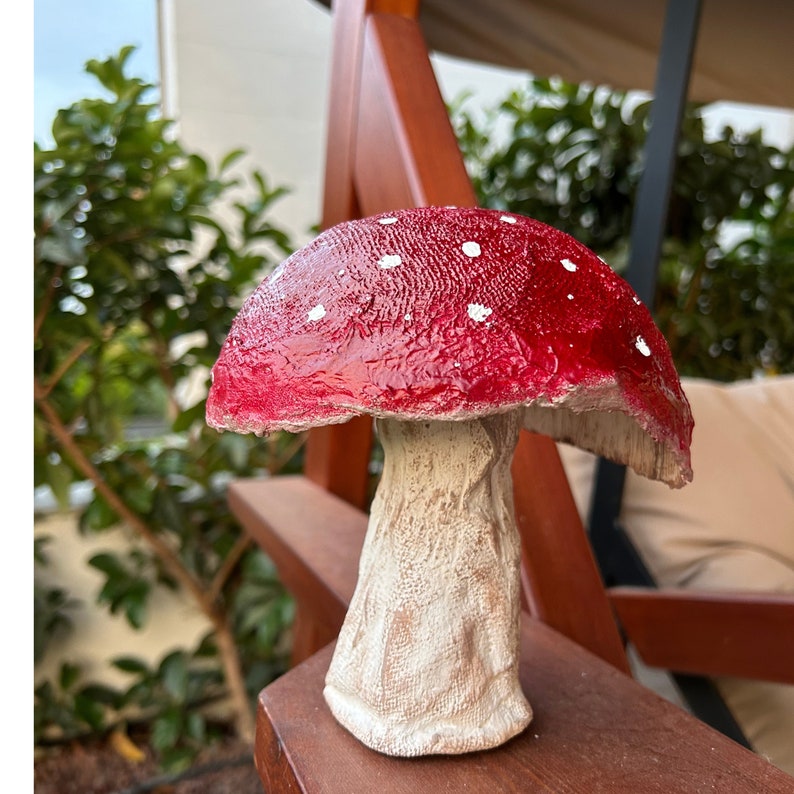 May include: A red and white mushroom garden statue with white polka dots on the top. The mushroom has a white stem with a textured surface.