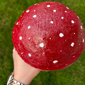 May include: A red and white mushroom with white spots. The mushroom is made of a smooth, shiny material.