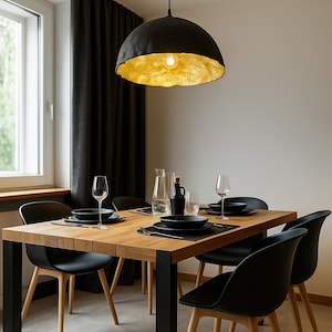 May include: A modern dining room with a black and gold pendant light hanging over a wooden table with black chairs. The table is set with black plates, glasses, and silverware.