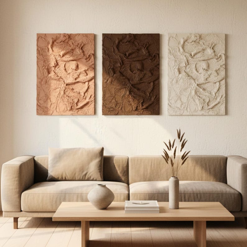 May include: Three textured wall art panels in beige, brown, and off-white hang above a beige sofa. The art has a crumpled paper effect. A wooden coffee table and decorative vase complete the living room setting.