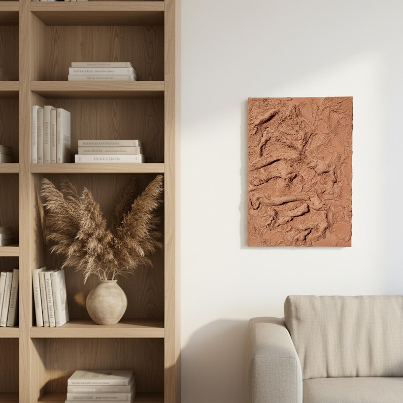 May include: A terracotta-coloured, rectangular textured wall art piece. The artwork features a raised, organic design, reminiscent of a topographical map or abstract landscape. It's mounted on a white wall, adding a modern touch to the room's decor.
