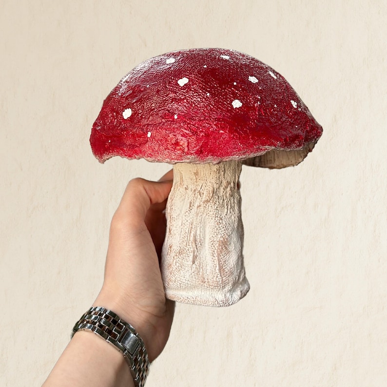 May include: A red and white mushroom with white spots on the cap. The mushroom is made of a textured material and has a white stem.