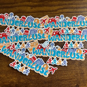 May include: A collection of stickers with the word "WANDERLUST" in a blue, bubble-style font. The stickers feature travel-themed icons like airplanes, passports, and luggage. The stickers are arranged on a wooden surface.