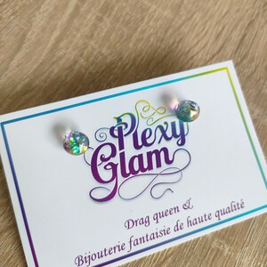 May include: A pair of iridescent rainbow stud earrings on a white card with the text "Plexy Glam Drag queen & Bijouterie fantaisie de haute qualité".