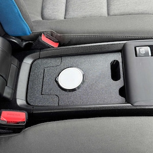 Könnte beinhalten: Ein schwarzer Auto-Konsolen-Organizer mit einem silbernen, kreisförmigen Deckel. Der Organizer ist in den Innenraum des Autos eingesetzt, mit einem roten "PRESS"-Knopf sichtbar. Der Innenraum ist grau und schwarz.