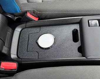 May include: A black car console organizer with a silver lid and a rectangular storage area. The console is installed between the front seats of a car. A red button with the word "PRESS" is visible.