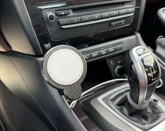 May include: A black car phone mount with a white circular phone holder. The mount is attached to the center console of a car.