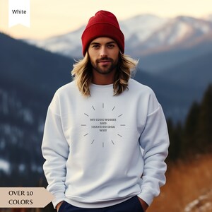 May include: White sweatshirt with the text "My code works and I have no idea why" in a circle with radiating lines. The sweatshirt is being worn by a person with long hair and a red beanie.