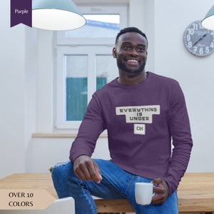 Może przedstawiać: Długi rękaw w kolorze fioletowym z nadrukiem "EVERYTHING IS UNDER Ctrl" na przodzie. Koszulka jest noszona przez osobę w luźnym otoczeniu.
